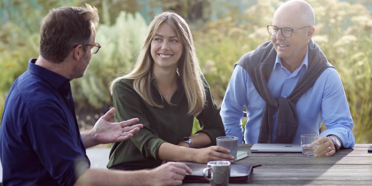 Three people sitting outside by a table.